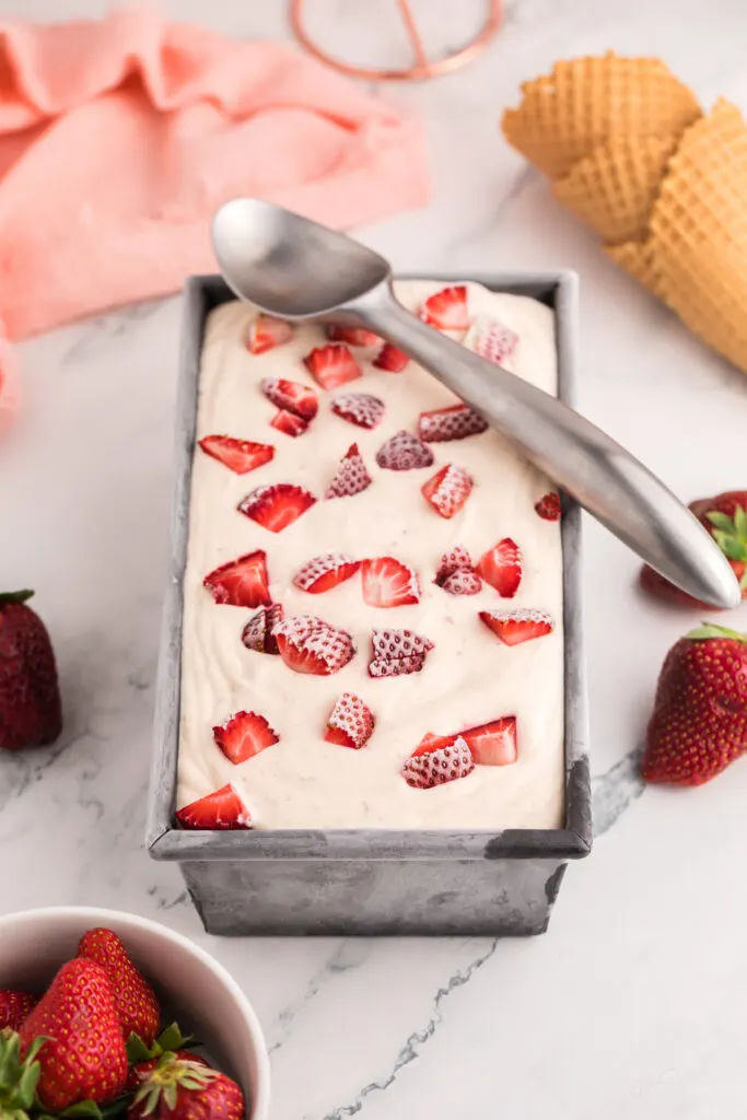Frozen strawberry ice cream in a loaf pan. There's an ice cream scoop on top.