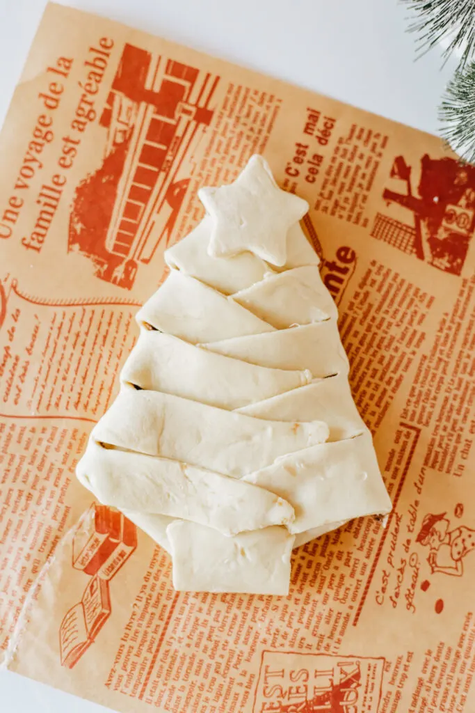 Puff pastry with a chocolate christmas tree in the center. The puff pastry is cut on the sides and bottom and is being folded over the chocolate. There is a star on top.