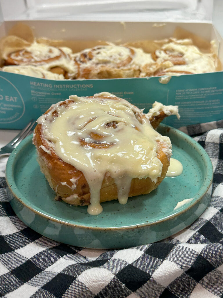 Cinnamon roll on a plate. There's a box of cinnamon rolls behind the plate. 