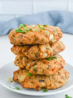 stacked salmon burgers on a white plate.