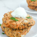 Air fryer salmon patties stacked on top of each other with a dollop of sour cream on top.