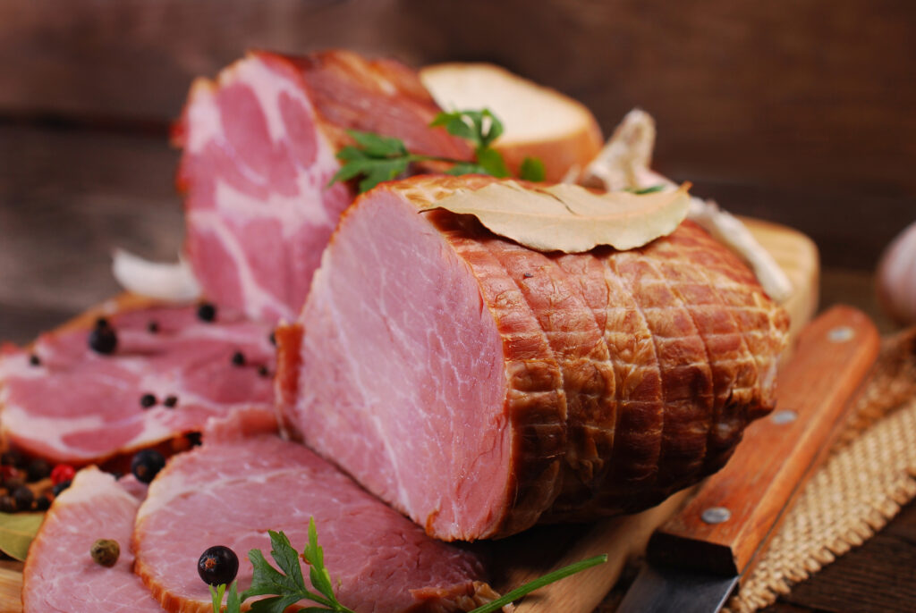 pieces of fresh homemade smoked ham with spices on rural background