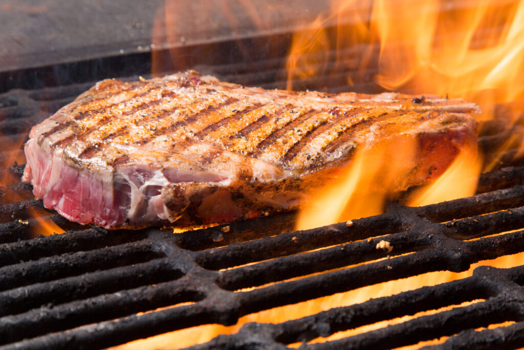 Raw bone in rib eye on a grill with flames in a grill pan
