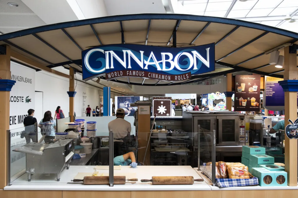 Cinnabon store sign above the store with people in it. 
