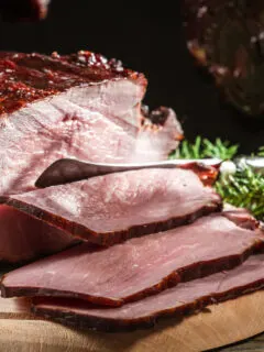 Closeup of a sliced piece ​​smoked ham with some greenery on the side.