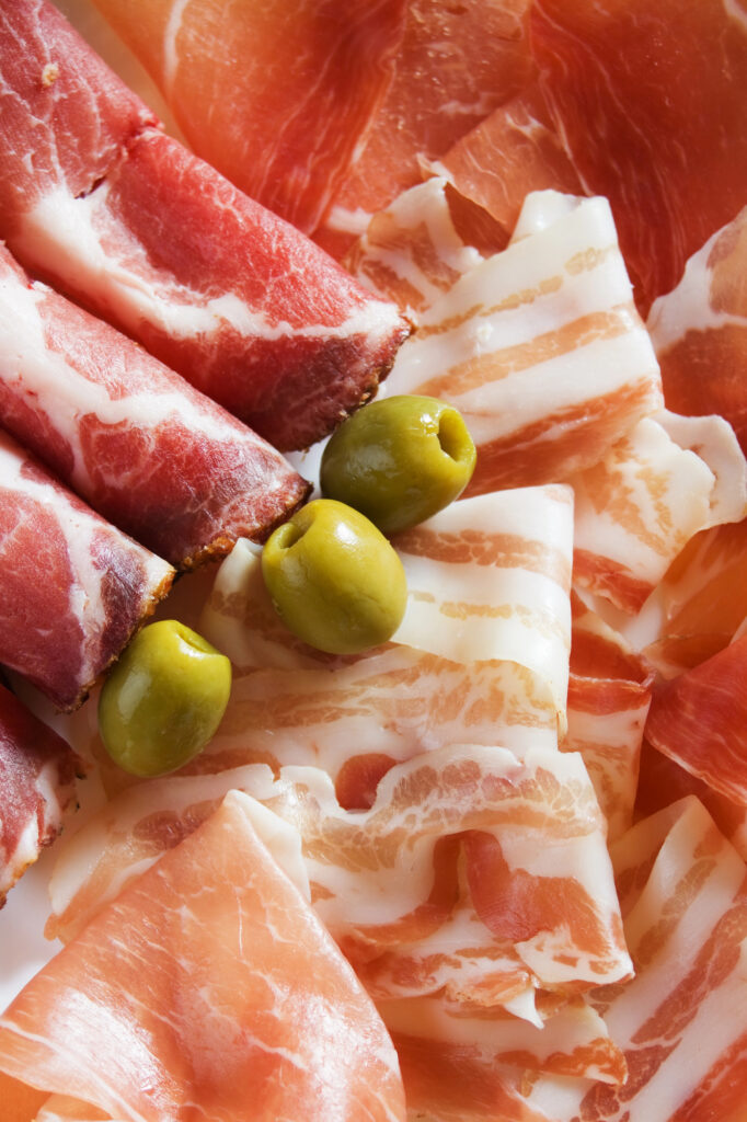 Prosciutto and olives on a plate.