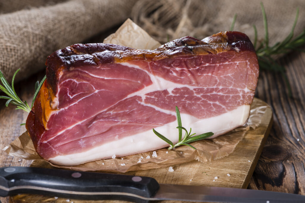 Sliced Smoked Ham with some fresh herbs on rustic wooden background