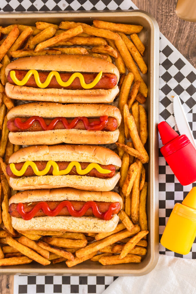 Hot dogs sitting on a cookie sheet with french fries. 