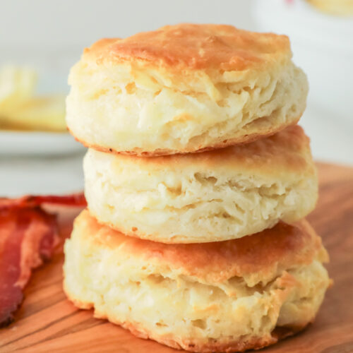 Fluffy biscuits stacked on a wooden cutting board.