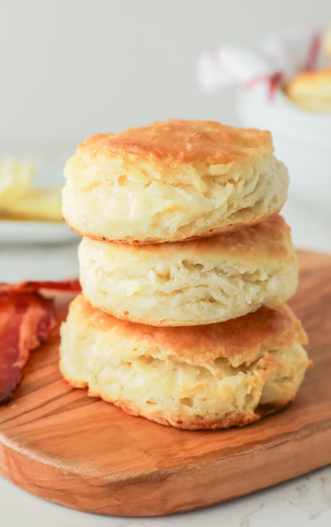 Fluffy biscuits stacked on a wooden cutting board. 